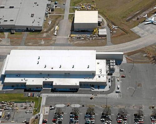 Aerial view of Gulfstream Paint Hangar. White building surrounded by vehicle parking lots and aircraft parked on apron.