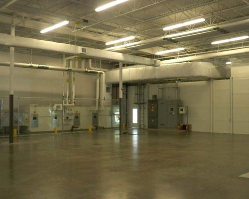 Interior of Gulfstream Paint Hangar. Large empty room with white walls, concrete floors, HVAC and exhaust ducts and fluorescent lighting.