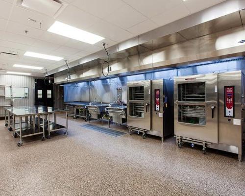 Interior photo of large room with stainless steel equipment: tables, sinks, shelving, ovens.