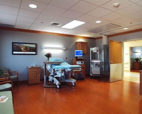 Interior photo of large hospital bedroom. Wood floors and cool grey walls.