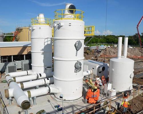 Two large white cylinders with piping along the ground and construction in the background