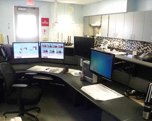 Interior photo of a workstation with 3 monitors. Upper cabinets and exit door are in the background.